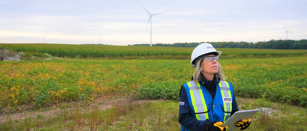 Employee in field with wind turbine in background