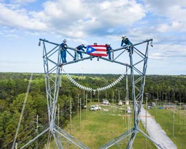 LUMA linemen present flag on top of transmission tower